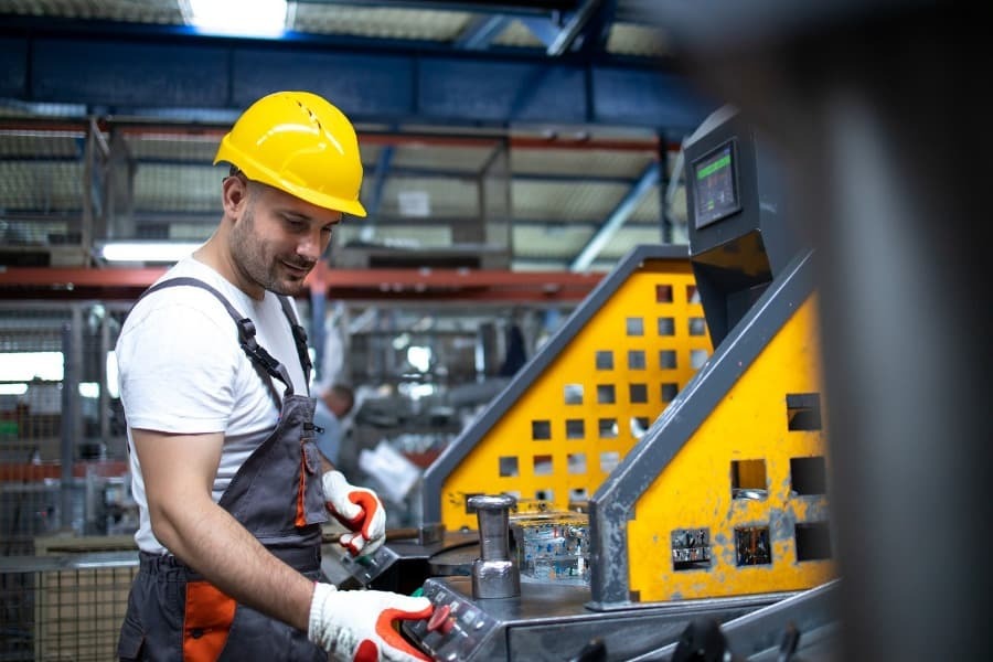 homem vestido de EPIs apertando botão de emergencia de maquina industrial